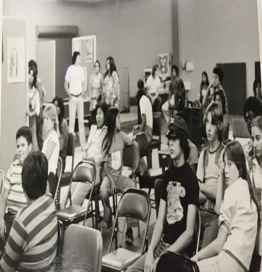Black and white photo from the 70's of a large group of people in a meeting room.